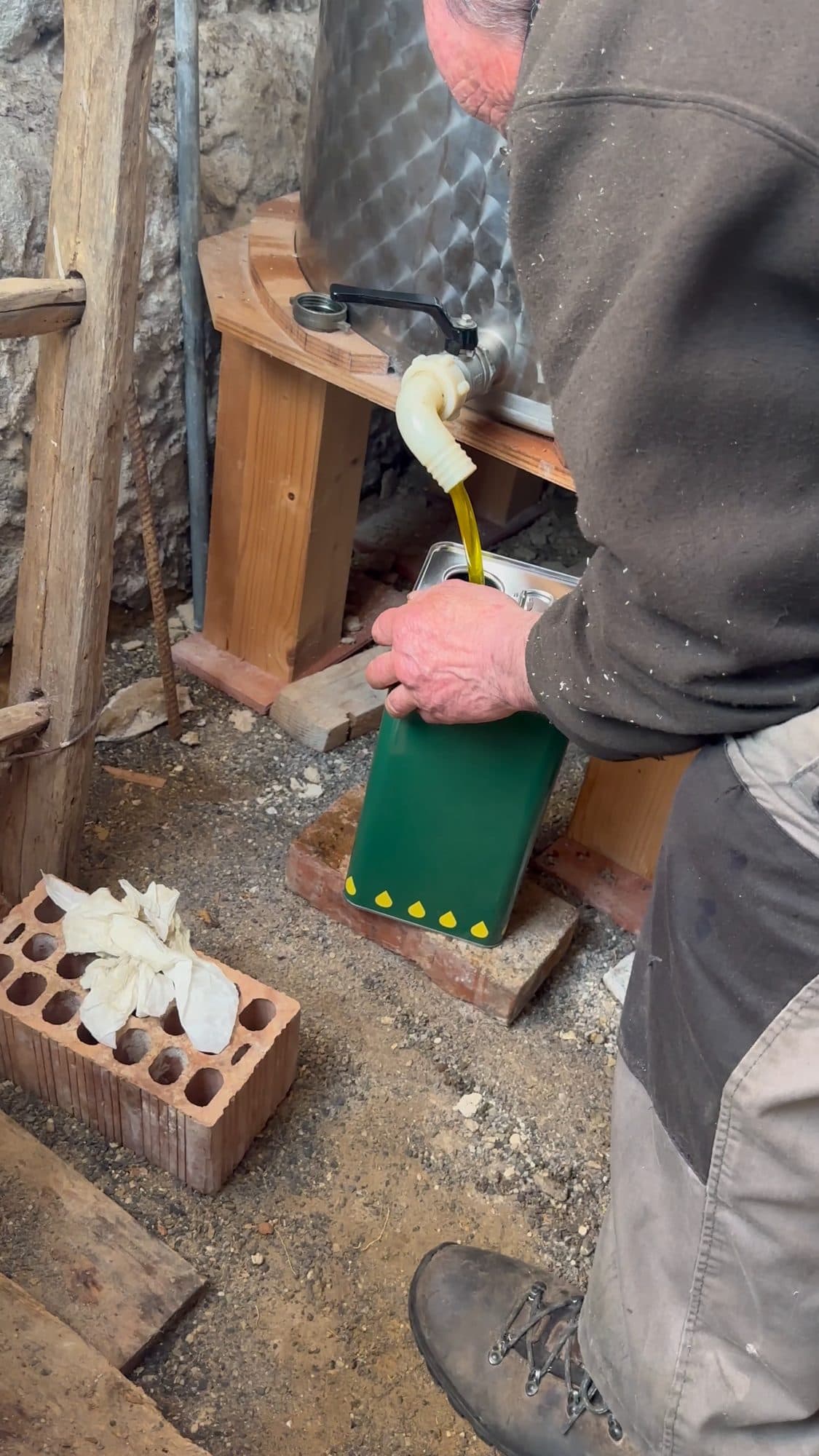 Olive oil pouring from the mill into a green tin.